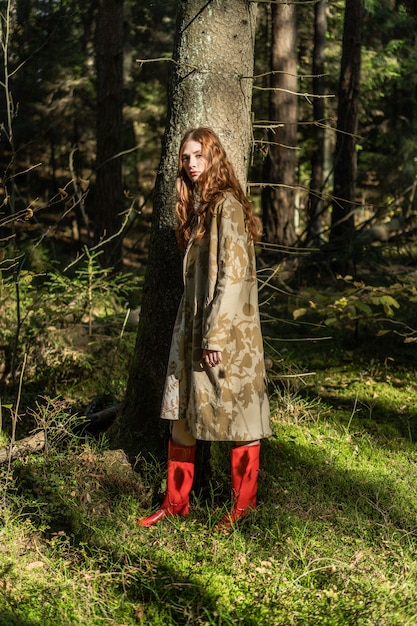 Giovane donna con lunghi capelli rossi in un vestito di lino raccolta funghi nella foresta