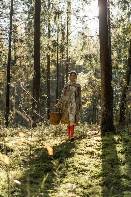 Giovane donna con lunghi capelli rossi in un vestito di lino raccolta funghi nella foresta