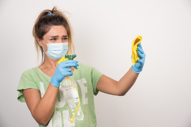 Giovane donna con maschera facciale che spruzza su un panno sul muro bianco.