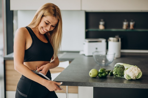 Giovane donna con nastro di misurazione sul weist in cucina