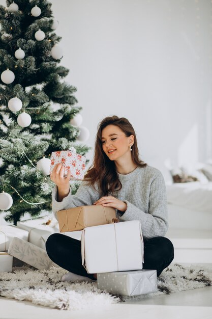 Giovane donna con regali di Natale dall'albero di Natale