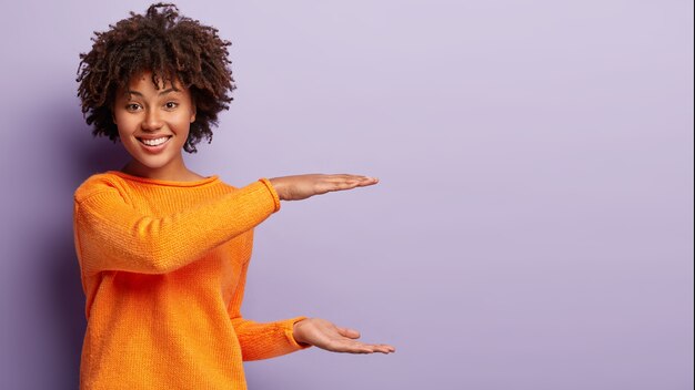 Giovane donna con taglio di capelli afro che indossa un maglione arancione