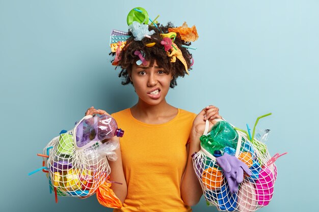 Giovane donna con taglio di capelli afro che tiene il sacchetto con i rifiuti di plastica