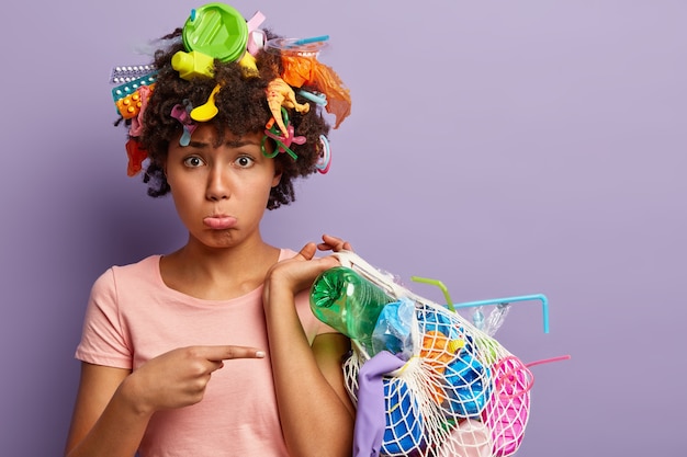 Giovane donna con taglio di capelli afro e rifiuti di plastica tra i capelli