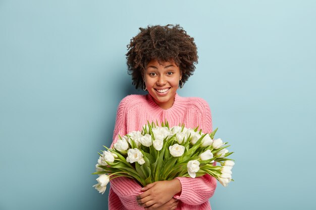 Giovane donna con taglio di capelli afro holding bouquet di fiori bianchi