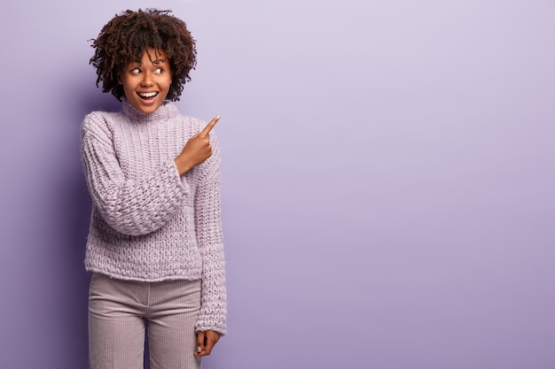 Giovane donna con taglio di capelli afro indossa un maglione viola