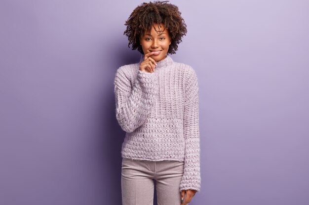Giovane donna con taglio di capelli afro indossa un maglione viola