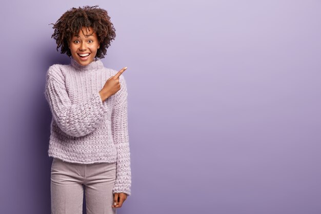 Giovane donna con taglio di capelli afro indossa un maglione viola