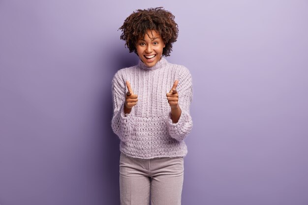 Giovane donna con taglio di capelli afro indossa un maglione viola