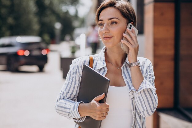 Giovane donna con telefono e computer che cammina fuori dalla strada