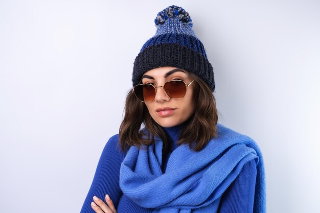 Giovane donna con un cappello da golf blu a collo alto e occhiali da sole sciarpa su sfondo bianco