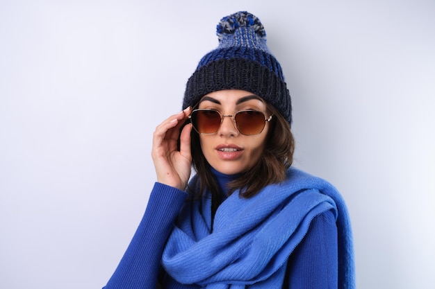 Giovane donna con un cappello da golf blu a collo alto e occhiali da sole sciarpa su sfondo bianco