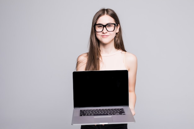 Giovane donna con un computer portatile che affronta la macchina fotografica isolata sopra la parete bianca