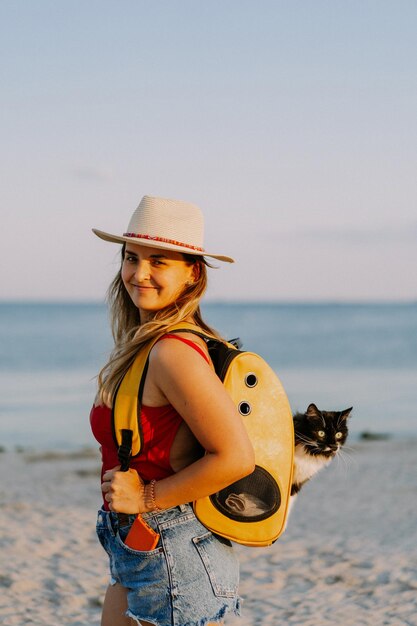 giovane donna con un gatto in uno zaino in riva al mare. Concetto di viaggio con un animale domestico. Gatto nello zaino con oblò.