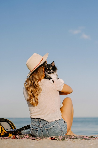 giovane donna con un gatto sulla spiaggia vicino al mare. Concetto di viaggio con un animale domestico.