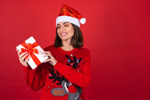 Giovane donna con un maglione natalizio e un cappello da Babbo Natale con una confezione regalo