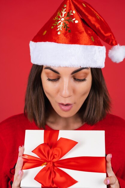 Giovane donna con un maglione natalizio e un cappello da Babbo Natale con una confezione regalo