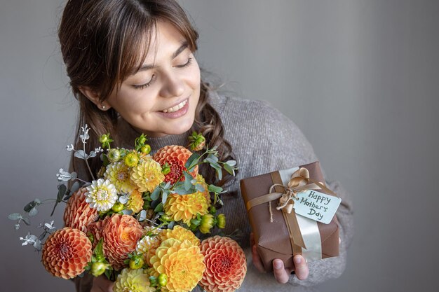 Giovane donna con un regalo per la festa della mamma e un mazzo di fiori in mano