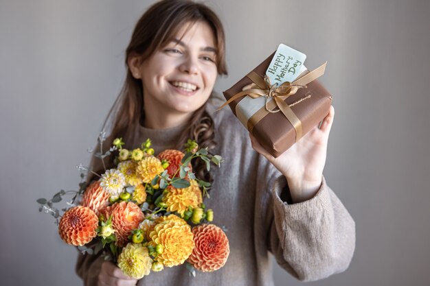 Giovane donna con un regalo per la festa della mamma e un mazzo di fiori nelle sue mani