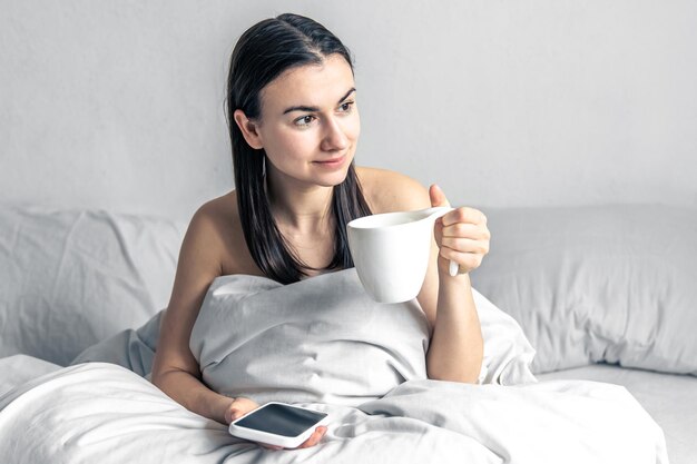 Giovane donna con uno smartphone e una tazza di caffè in mano