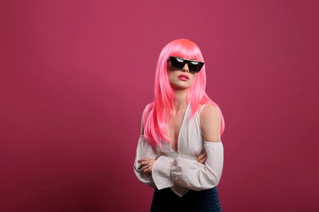 Giovane donna con uno stile di moda elegante che indossa occhiali da sole alla moda, con un atteggiamento sicuro e sexy con i capelli rosa. Sentirsi spensierati e sensuali con occhiali moderni ed eleganti in studio.