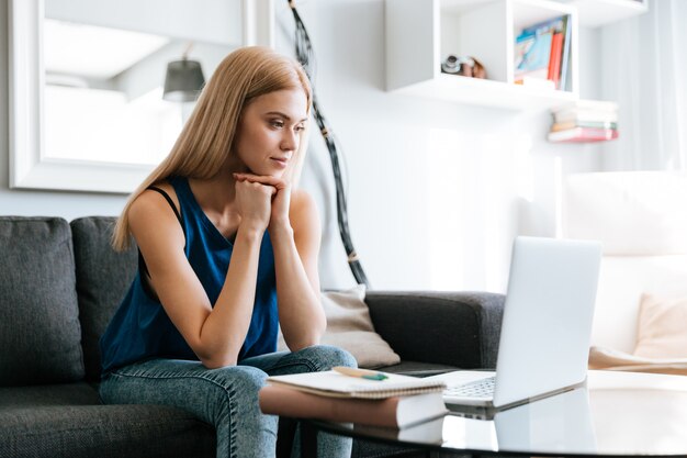 Giovane donna concentrata che si siede e che lavora con il computer portatile a casa