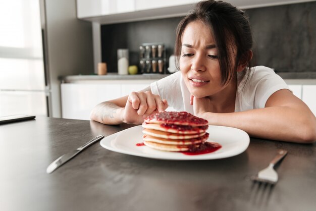 Giovane donna confusa che si siede alla cucina nella casa