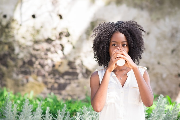 Giovane donna consapevole che beve caffè all&#39;aperto