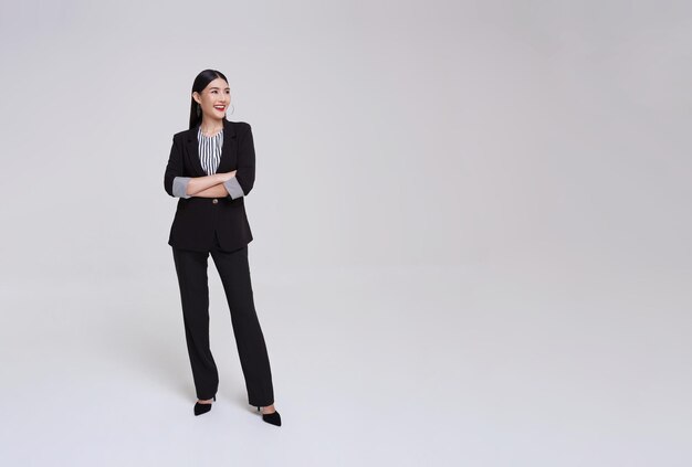 Giovane donna d'affari asiatica in abito con le braccia incrociate e un sorriso in postura in piedi
