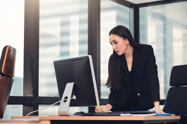 Giovane donna d'affari asiatica intelligente per adulti in abito casual nero che lavora con il computer in ufficio urbano