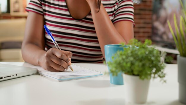 Giovane donna d'affari che lavora a distanza e prende appunti, imparando una lezione di classe sulla connessione di rete online. Utilizzo di laptop e notebook per partecipare al webinar in remoto dall'home office.