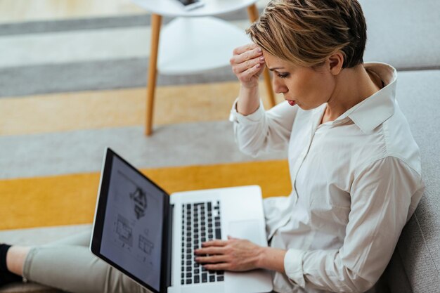Giovane donna d'affari che si sente frustrata durante la lettura di e-mail problematiche su un computer a casa