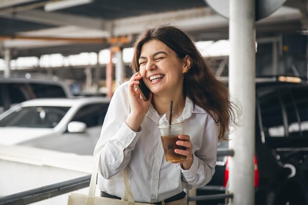 Giovane donna d'affari con caffè che parla allegramente al telefono nel parcheggio