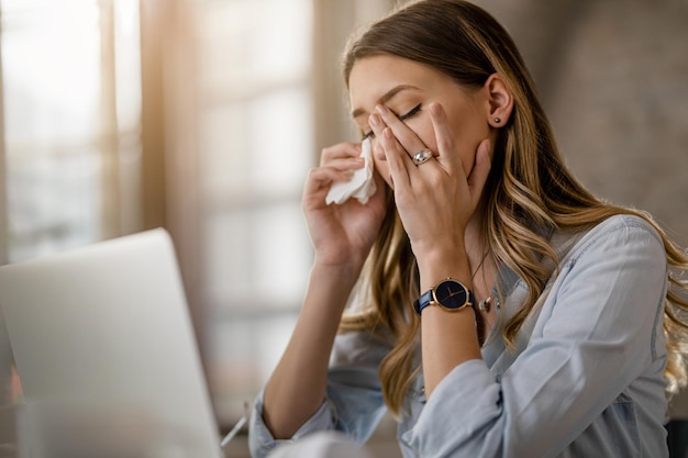 Giovane donna d'affari con virus del raffreddore e dell'influenza che ha mal di testa mentre lavora in ufficio
