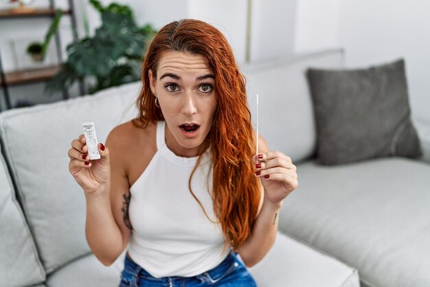 Giovane donna dai capelli rossi che esegue un test nasale per l'infezione da coronavirus con un'espressione confusa e incapace. concetto di dubbio.