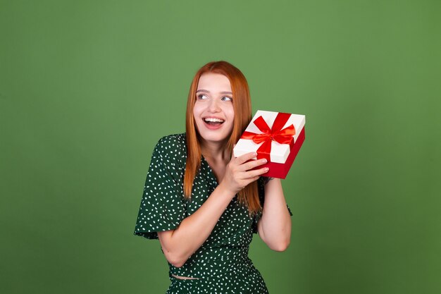 Giovane donna dai capelli rossi sulla parete verde con scatola regalo felice eccitata stupita sorpresa