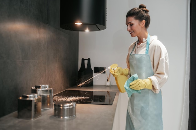 Giovane donna dai capelli scuri che disinfetta le superfici in cucina