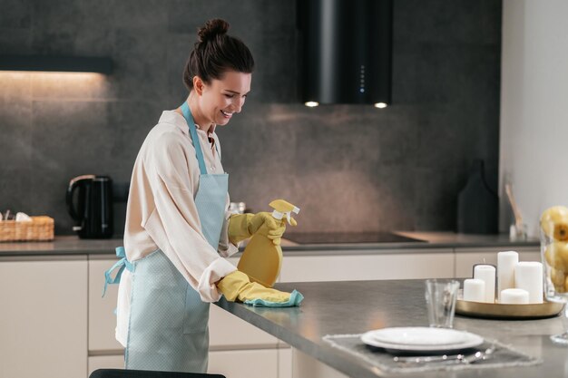 Giovane donna dai capelli scuri che disinfetta le superfici in cucina