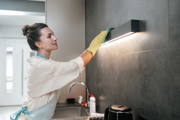 Giovane donna dai capelli scuri che pulisce la lampada in cucina