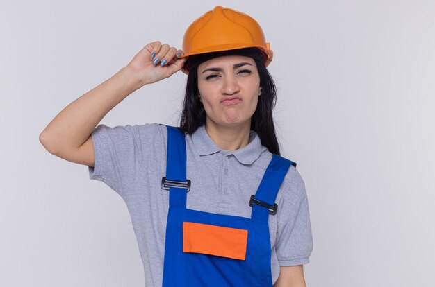 Giovane donna del costruttore in uniforme da costruzione e casco di sicurezza che guarda l'obbiettivo