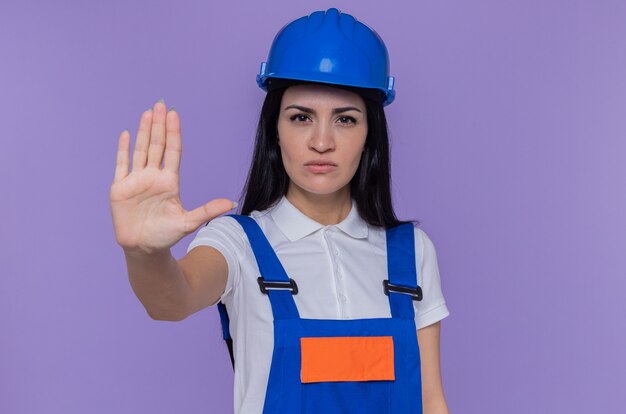 Giovane donna del costruttore in uniforme da costruzione e casco di sicurezza che guarda l'obbiettivo