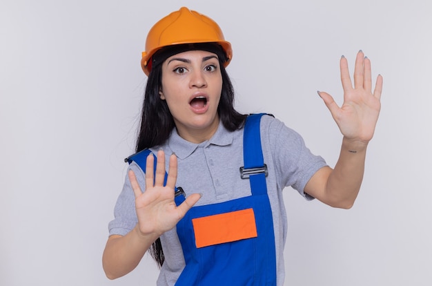 Giovane donna del costruttore in uniforme da costruzione e casco di sicurezza che sembra preoccupata