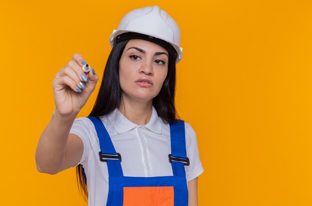 Giovane donna del costruttore in uniforme della costruzione e casco di sicurezza che osserva da parte