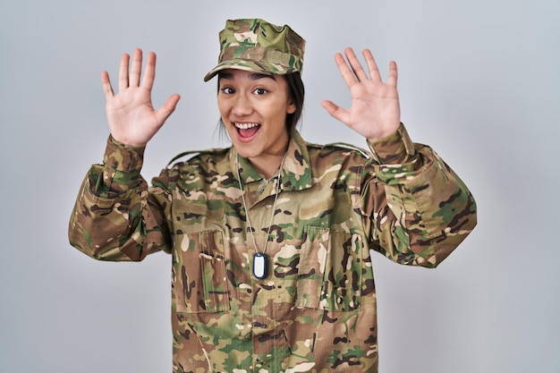 Giovane donna dell'Asia meridionale che indossa l'uniforme dell'esercito mimetico mostrando e indicando con le dita numero dieci mentre sorride fiducioso e felice.