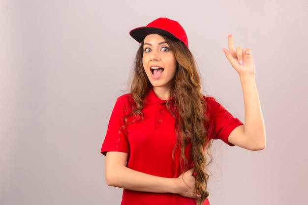 Giovane donna delle consegne che indossa la maglietta polo rossa e cappuccio che sembra sorpreso puntare il dito sul nuovo concetto di idea su sfondo bianco isolato