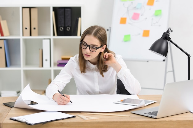 Giovane donna di affari che progetta il progetto su Libro Bianco nell&#39;ufficio