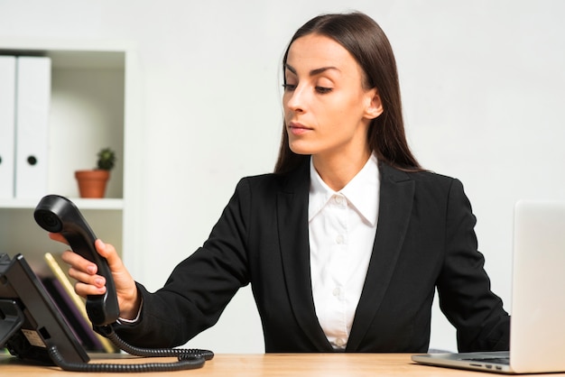 Giovane donna di affari che si siede nell&#39;ufficio che dispone la ricevente del telefono