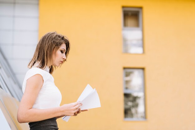 Giovane donna di affari che sta fuori i documenti della lettura dell&#39;ufficio