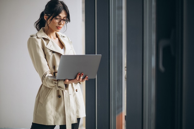 Giovane donna di affari con il computer portatile che fa una pausa la finestra in ufficio