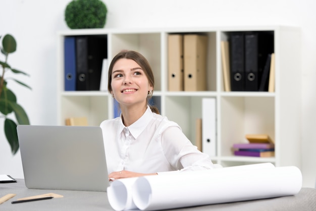 Giovane donna di affari felice che daydreaming mentre per mezzo del computer portatile nell&#39;ufficio